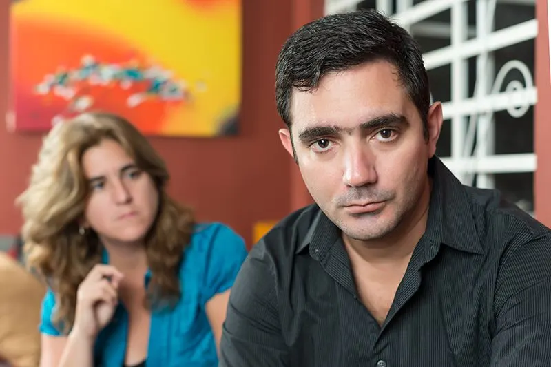 A man in the foreground looking at the camera with a woman out of focus behind him