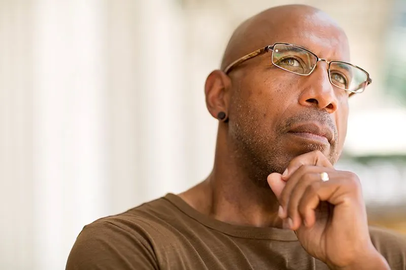 A man with glasses resting his hand at his chin, looking past the camera
